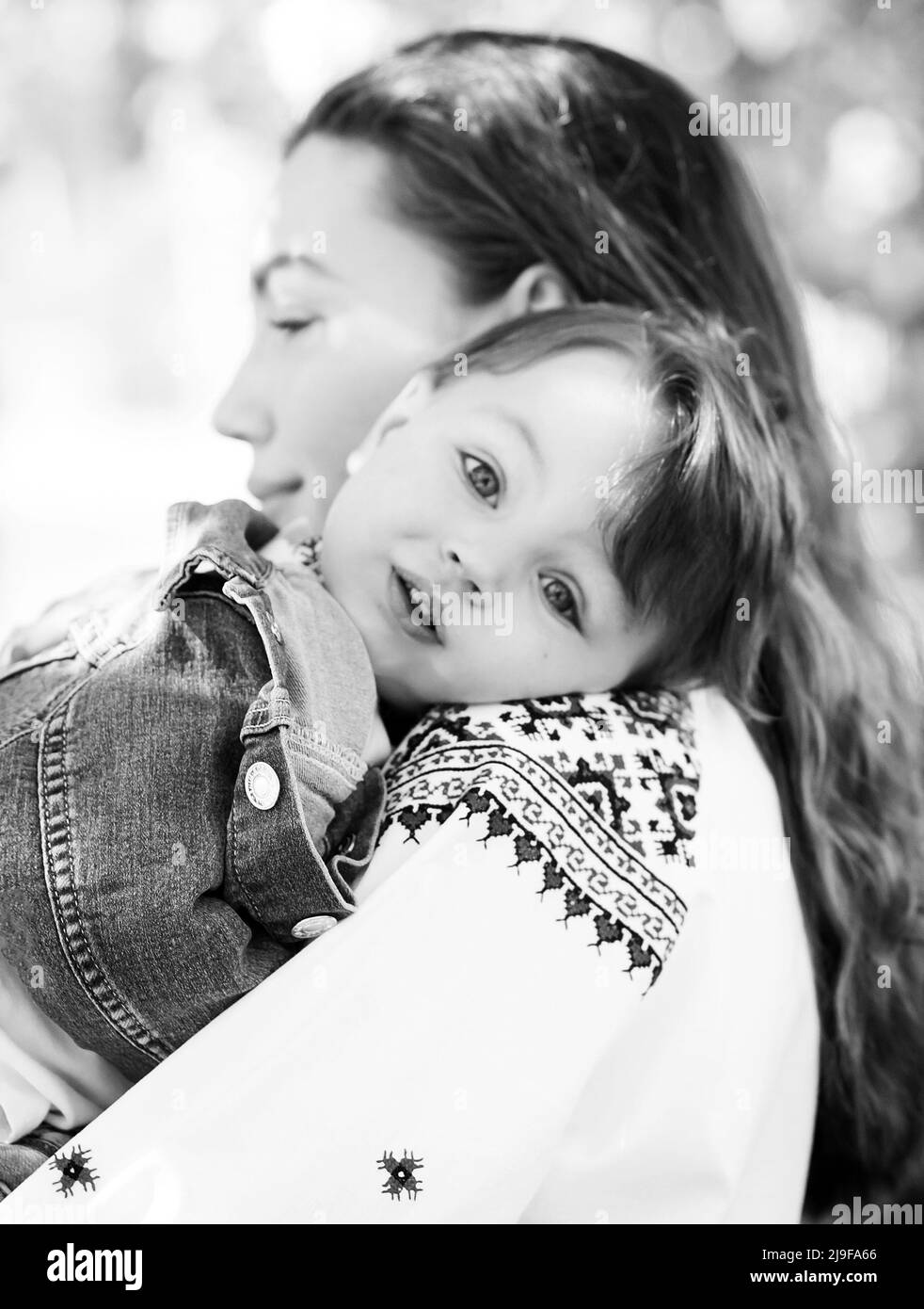 Schwarz-Weiß-Foto kleines Baby auf den Händen der Mutter. Porträt einer Familie von zwei Personen. Frühling Landschaft Hintergrund. Stockfoto
