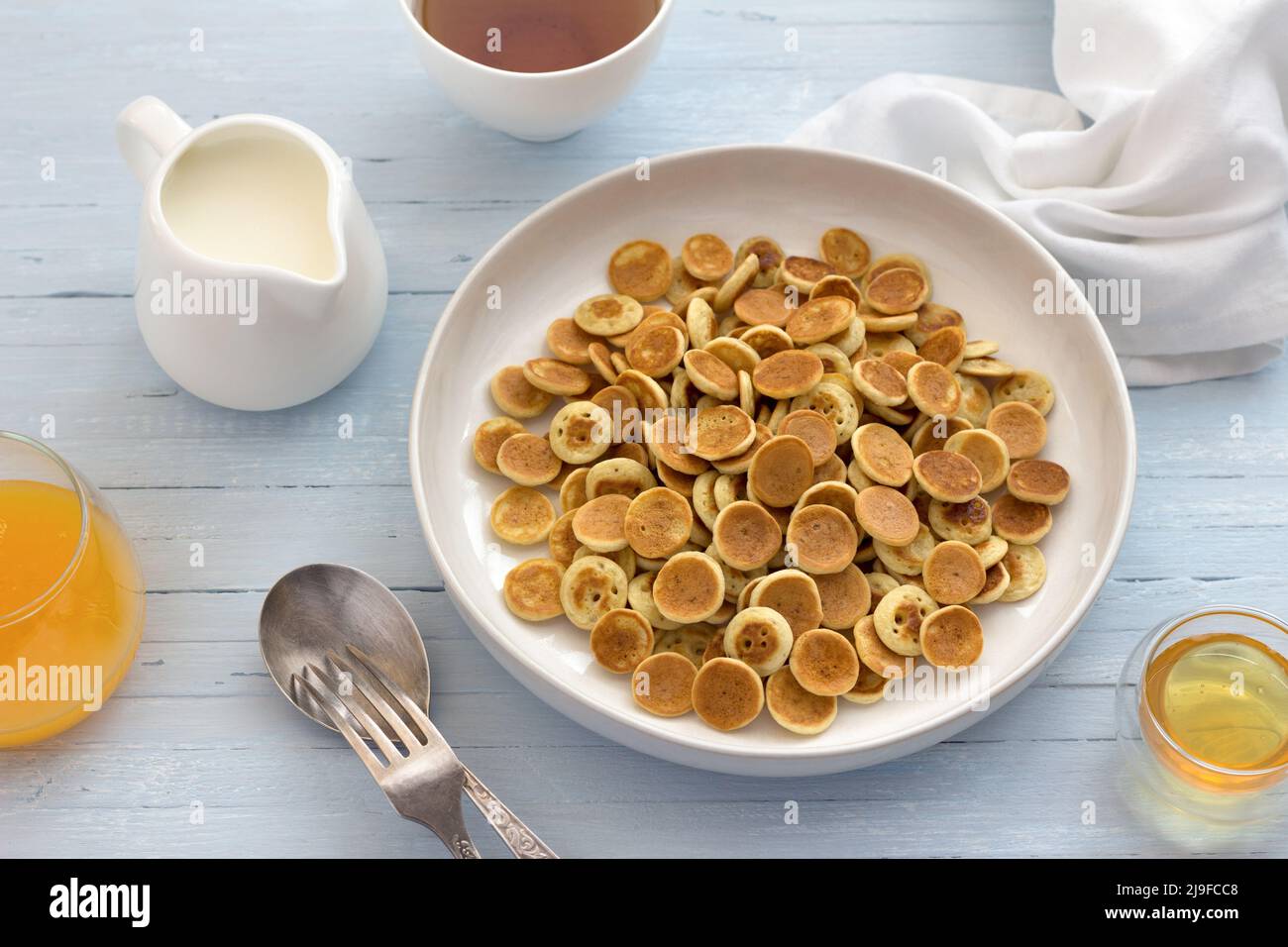Teller Mini Pancakes Müsli mit Honig, Creme und frischem Orangensaft auf hellblauem Hintergrund. Trendige Küche. Hausgemachtes Frühstück. Draufsicht Stockfoto