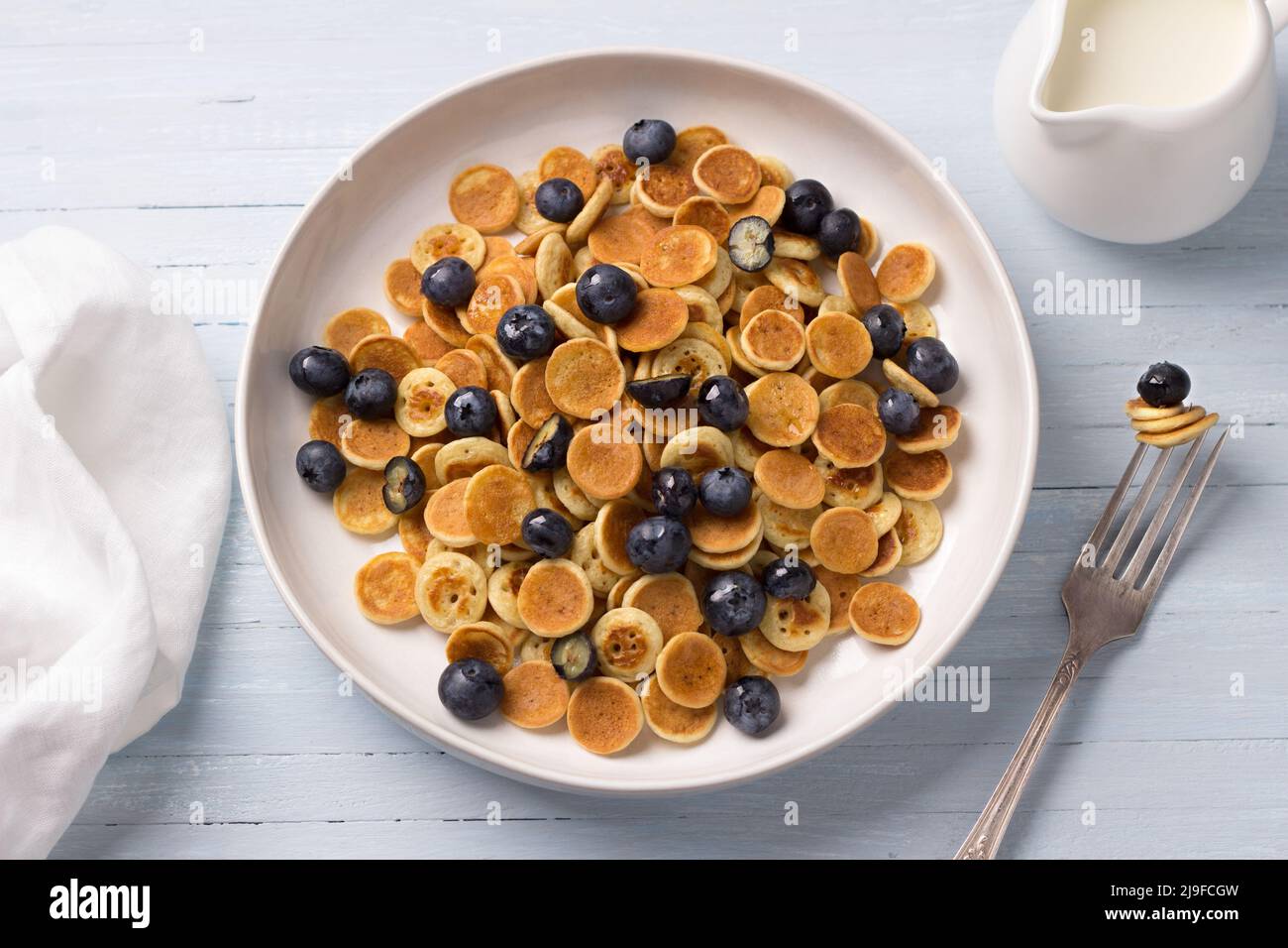 Teller Mini Pancakes Müsli mit Creme, Honig und Beeren auf einem hellblauen Hintergrund. Trendige Speisen. Hausgemachtes Frühstück. Draufsicht Stockfoto