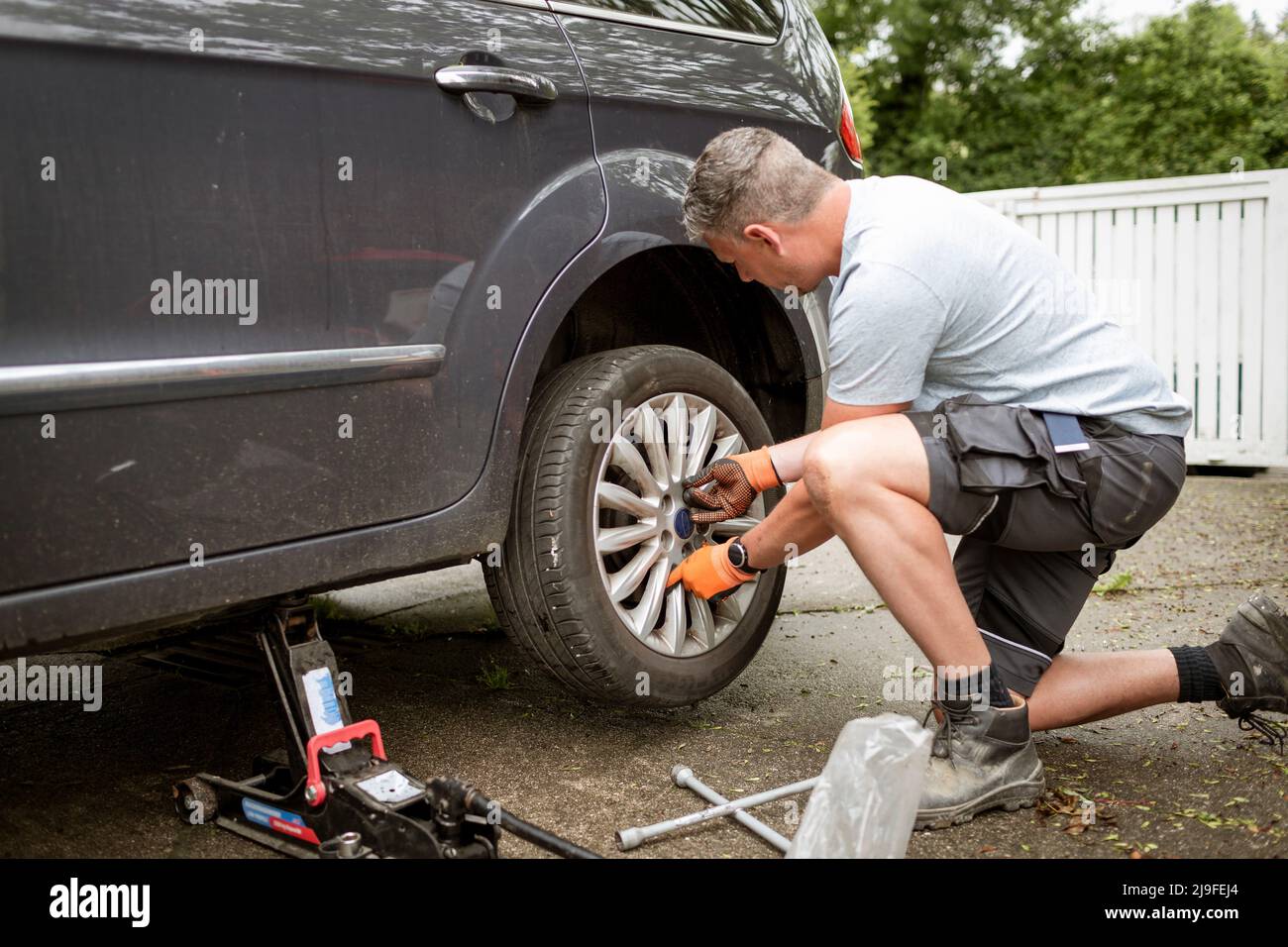 Mann mittleren Alters mit grauen Haaren wechselt die Reifen auf seinem Familienwagen Stockfoto