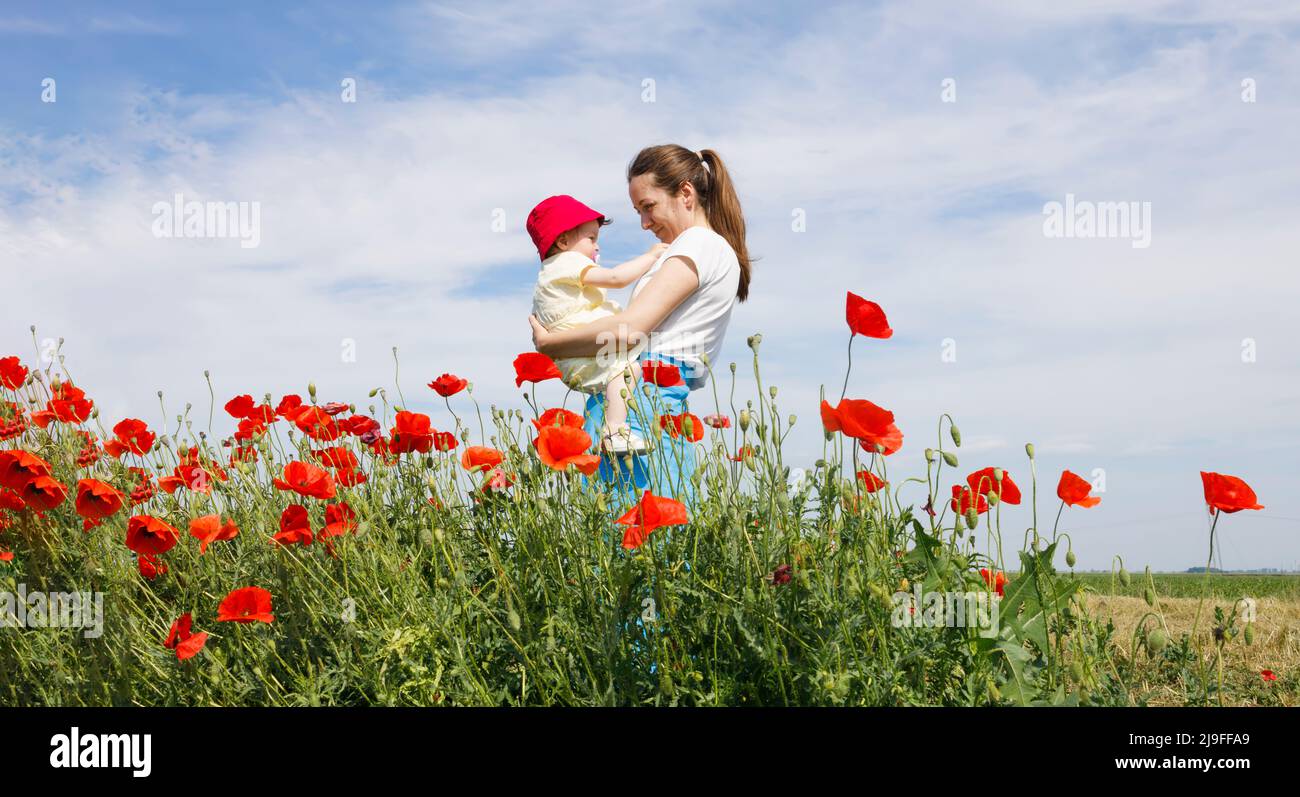 Eine Frau, die ihr Kind auf einem Feld aus rotem Mohn hält Stockfoto