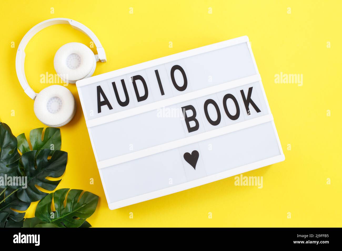 Die Inschrift Hörbuch auf einem Leuchtkasten mit modernen weißen Kopfhörern auf einem gelben Hintergrund. Hören eines Buches. E-Learning. Stockfoto