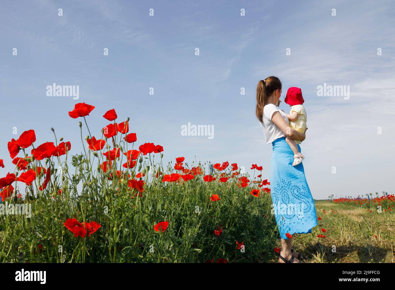 Eine Mutter, die ihre Tochter auf einer Wiese voller Mohnblumen trägt Stockfoto