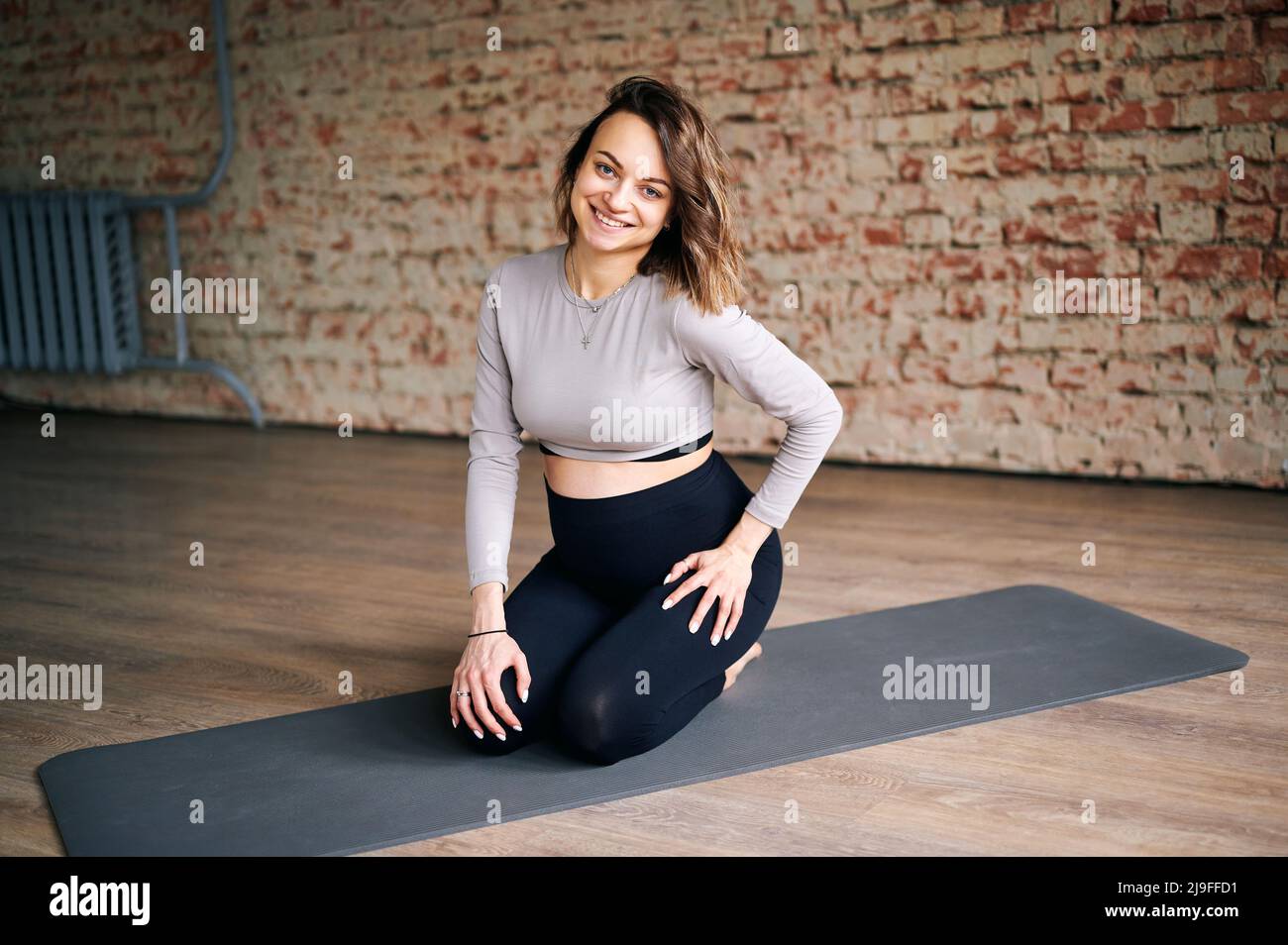 Junge Schwangerin, die nach dem Yoga-Unterricht auf der Matte sitzt. Zukünftige Mutter kümmert sich um gesunde und praktiziert Dehnübungen in Innenräumen Stockfoto