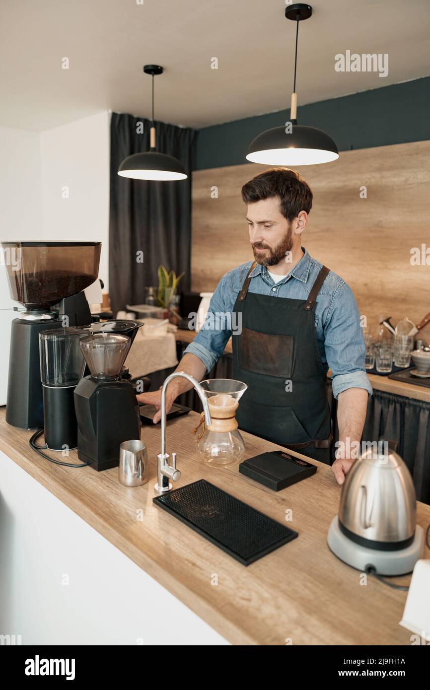 Der gutaussehende Barista mahlt Kaffeebohnen in der Kaffeemaschine Stockfoto