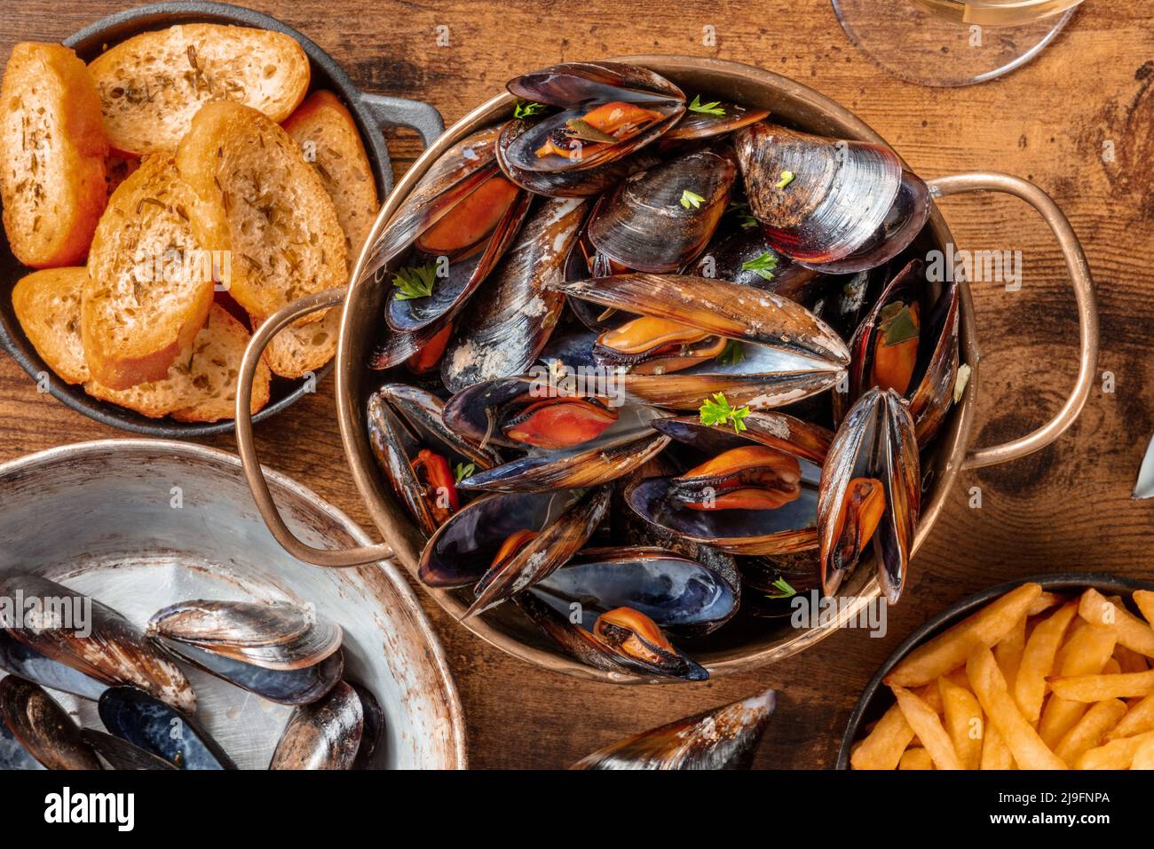 Belgische Muscheln mit Pommes frites und geröstetem Brot, über dem Kopf flach auf einem rustikalen Holzhintergrund Stockfoto