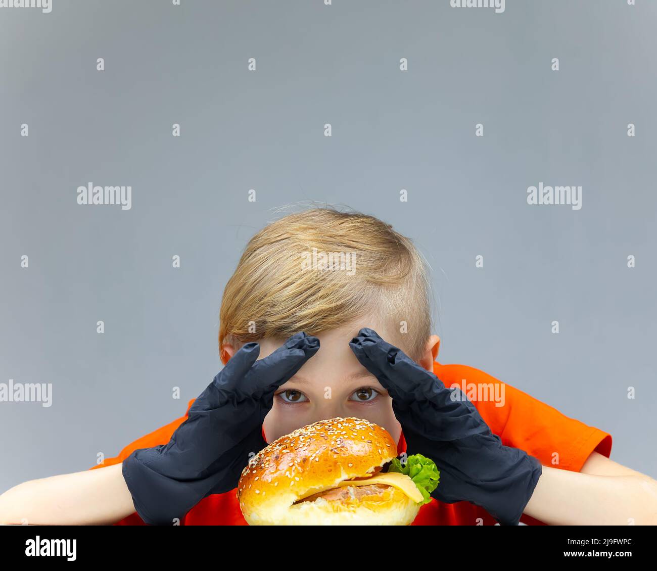 Der Junge mit dem Cheeseburger lehnt sich über ihn, umklappt seine Hände und schaut durch den Hamburger Stockfoto