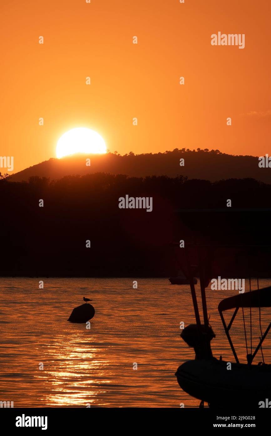 Ein weißes Segelboot segelt auf dem Meer mit einem orangefarbenen Sonnenuntergang Stockfoto