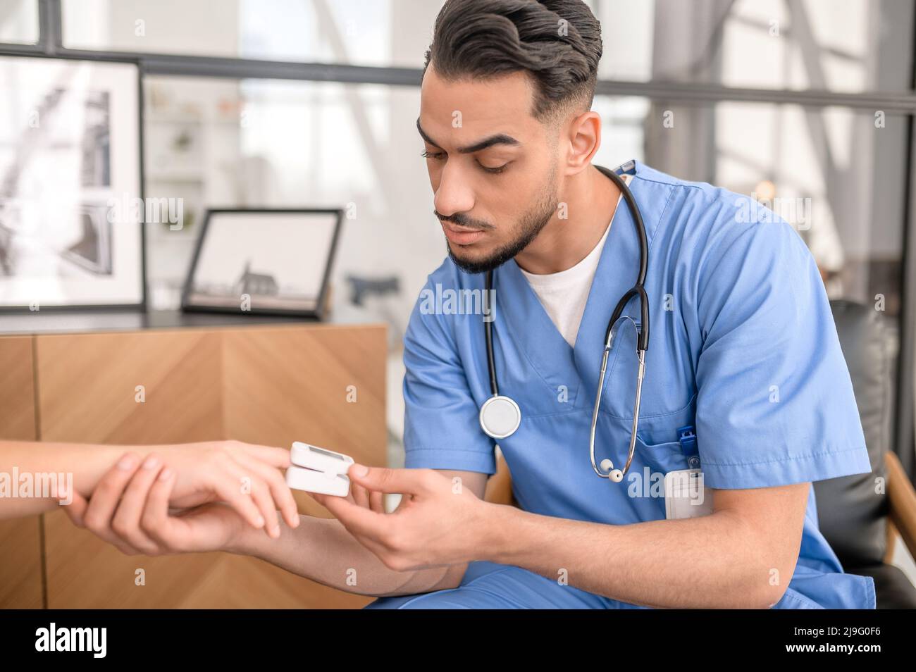 Konzentrierter Arzt, der ein Pulsoximeter auf die Fingerspitze einer Person legt Stockfoto