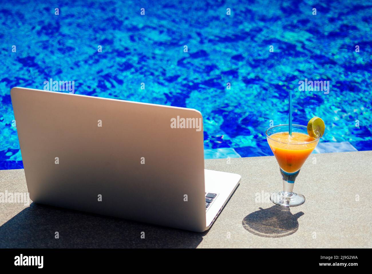 Alkoholfreier Smoothie-Cocktail aus Obst in einem Glas-Becher-Laptop am Pool, freiberufliche Fernarbeit im Urlaub und Frilansing-Konzept Stockfoto