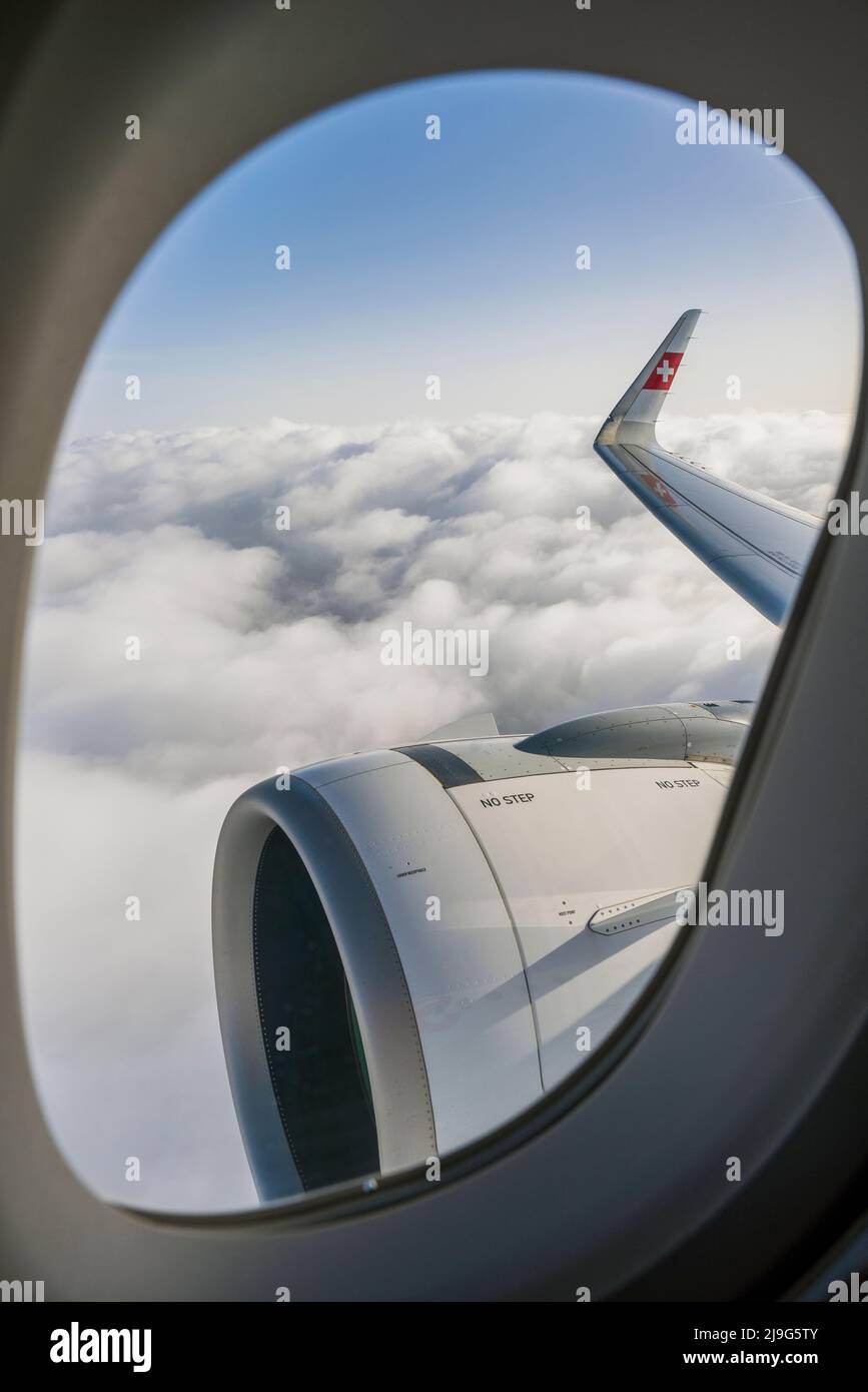 Fensteransicht des rechten Flügels und des Motors eines Schweizer Airbus A320-200 neo, der über den Wolken fliegt Stockfoto