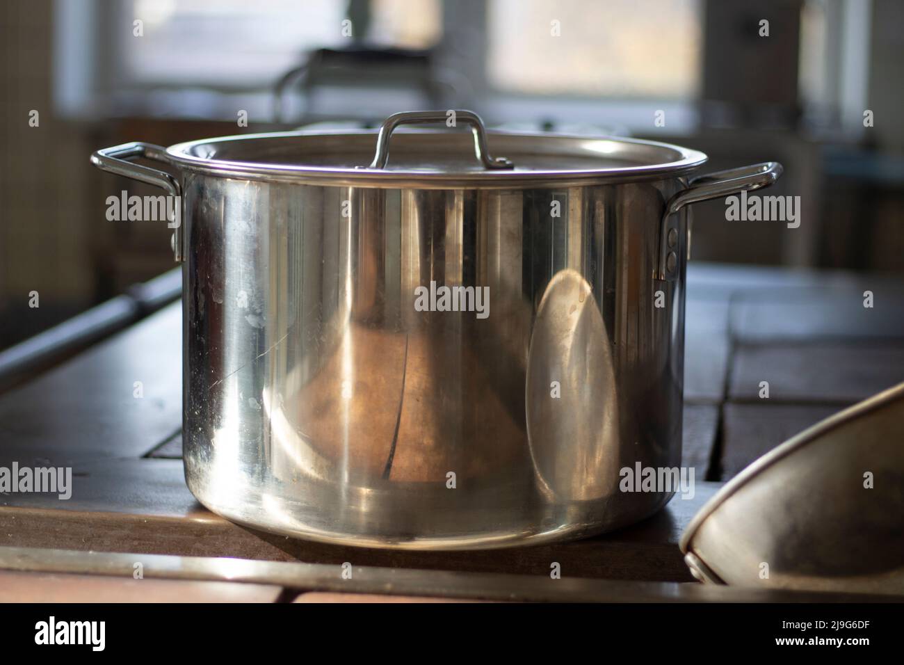 Großer Topf wird auf dem Herd erhitzt. Besteck in der Küche. Details zum Kochen im Esszimmer. Chrom-Pfanne im Sonnenlicht. Stockfoto