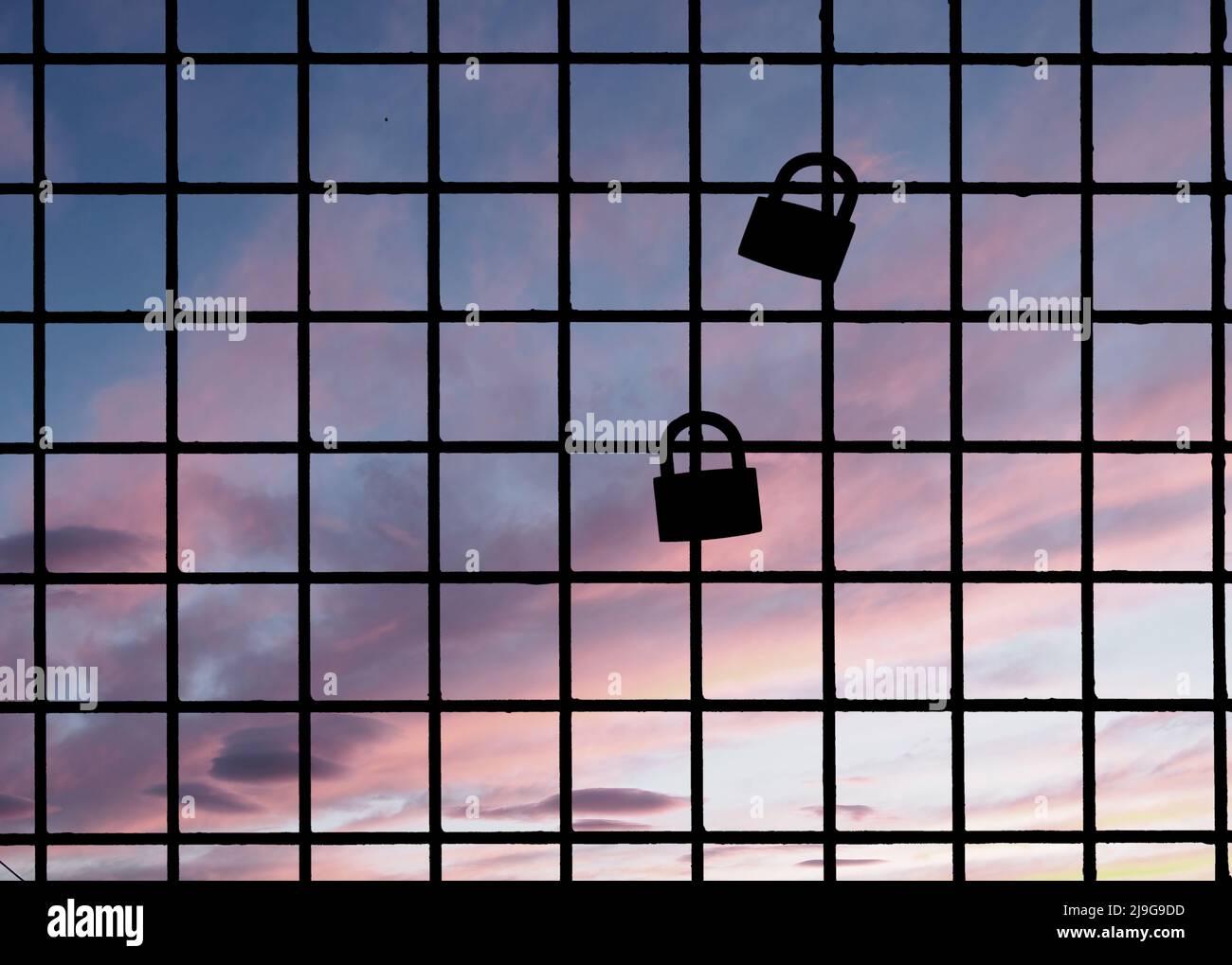 Zwei Vorhängeschlösser am Zaun, Silhouette gegen den Sonnenuntergang. Traditionelles Liebessymbol. Stockfoto