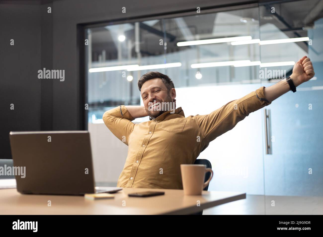 Zufriedener Geschäftsmann In Der Nähe Von Laptop Stretching Arms Entspannendes Sitzen Im Büro Stockfoto