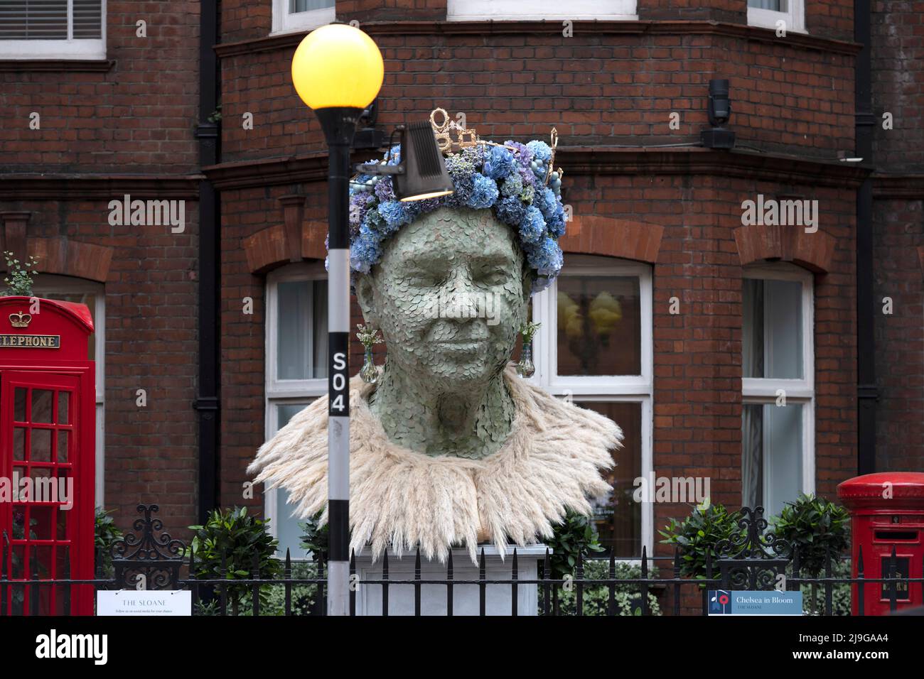 Lower Sloane Street, London, Großbritannien. 23 Mai 2022. Der Sommeranfang wird mit einem Besuch in Chelsea in Bloom gefeiert, Chelseas jährlich stattfindende Blumenkunstausstellung und Londons größtem, kostenlosen Blumenfestival, das zeitgleich mit der RHS Chelsea Flower Show stattfindet. Bild: Porträt der Königin mit traditionellen britischen Ikonen - rote Telefondose und rote Briefkasten - außerhalb der Sloane. Quelle: Malcolm Park/Alamy Live News Stockfoto