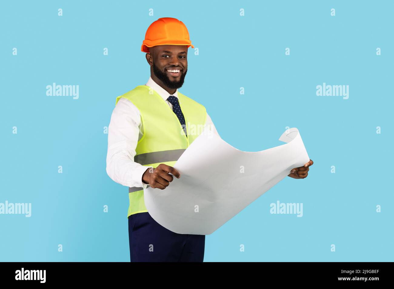Lächelnder Afroamerikanischer Auftragnehmer, Der Blueprints Hält, Während Er Isoliert Auf Blauem Hintergrund Steht Stockfoto
