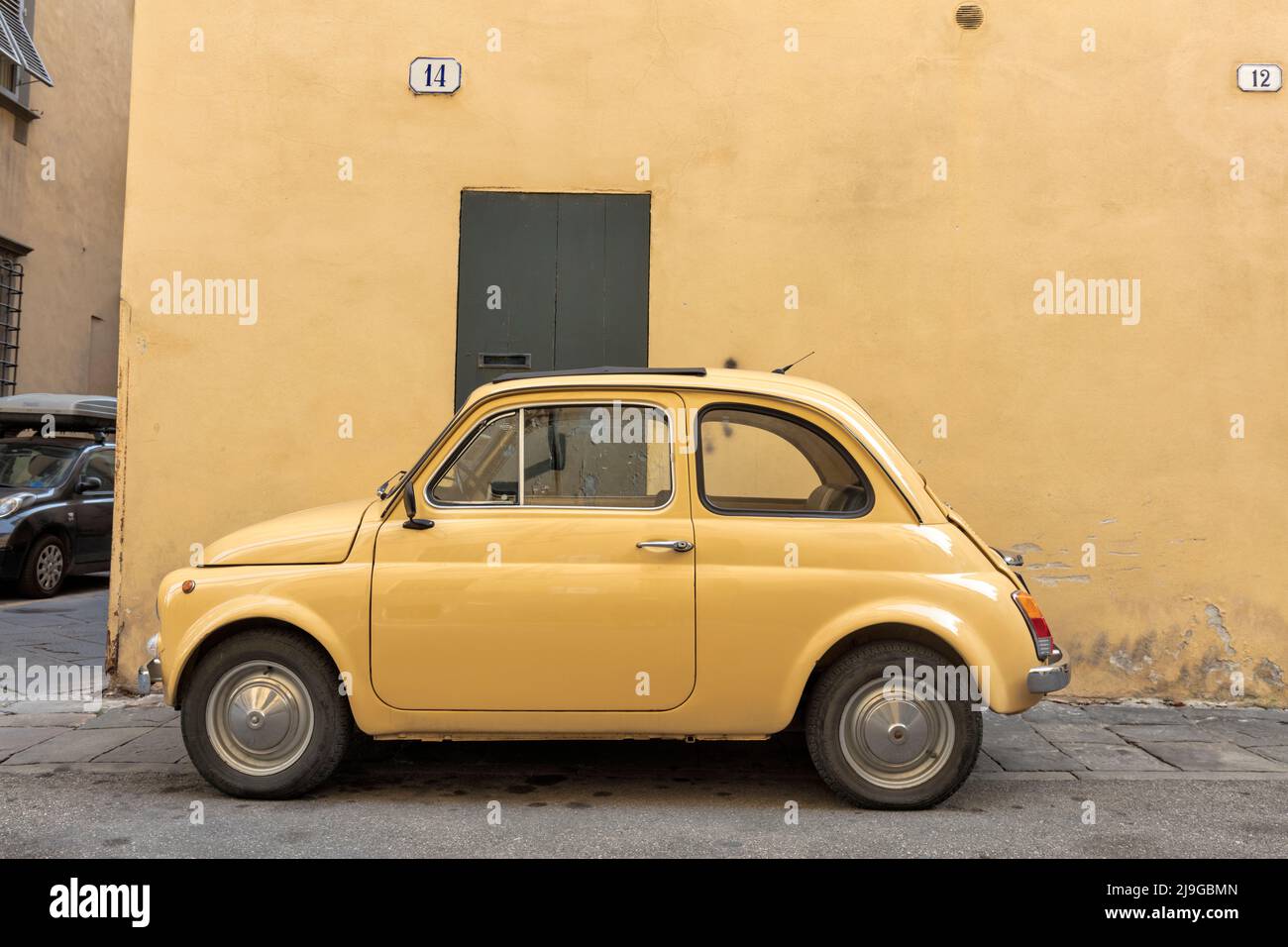 Gelbes Oldtimer Fiat 500 vor der gelben Mauer in einer engen Straße im mittelalterlichen Stadtzentrum von Lucca Stockfoto