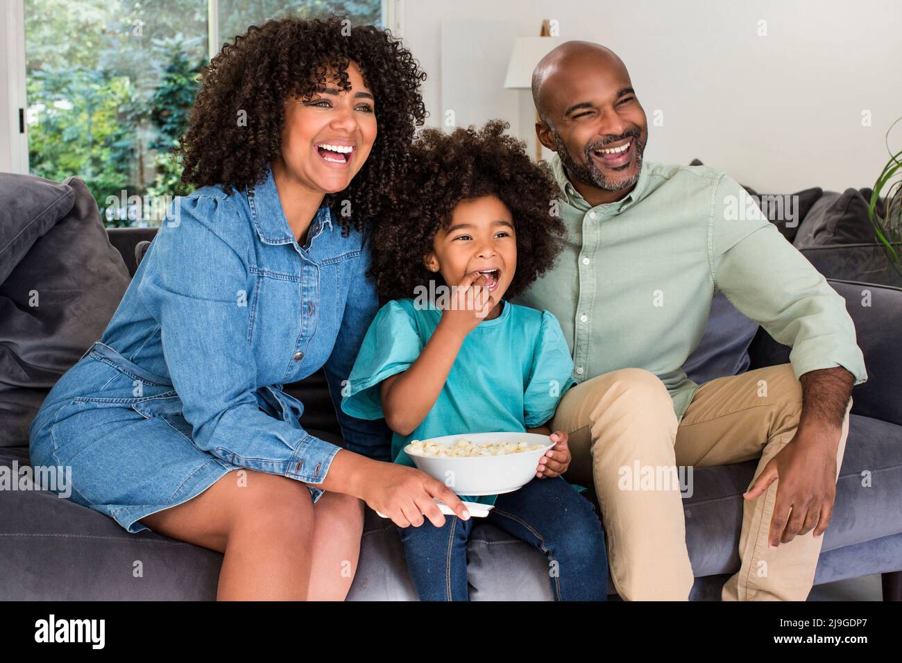 Glückliche Familie, die zusammen Fernsehen schaut, während sie auf dem Sofa sitzt Stockfoto