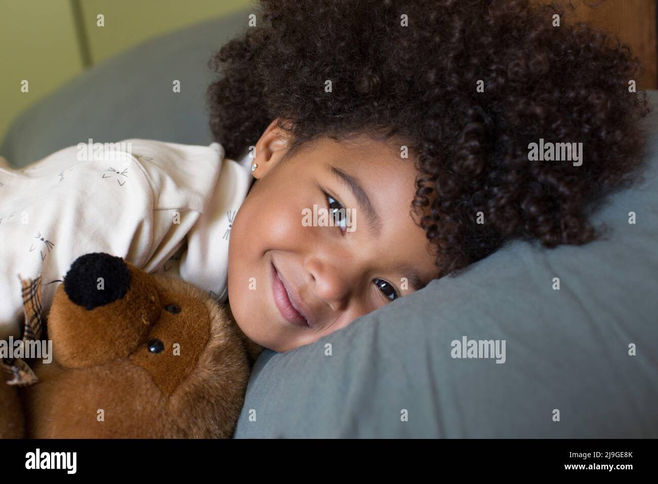 Lächelndes Mädchen liegt mit Spielzeug auf dem Bett Stockfoto