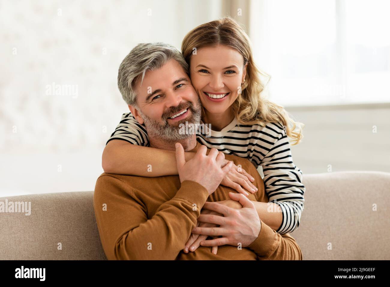 Liebevolles Paar Mittleren Alters Umarmt Sitzen Auf Sofa Zu Hause Stockfoto