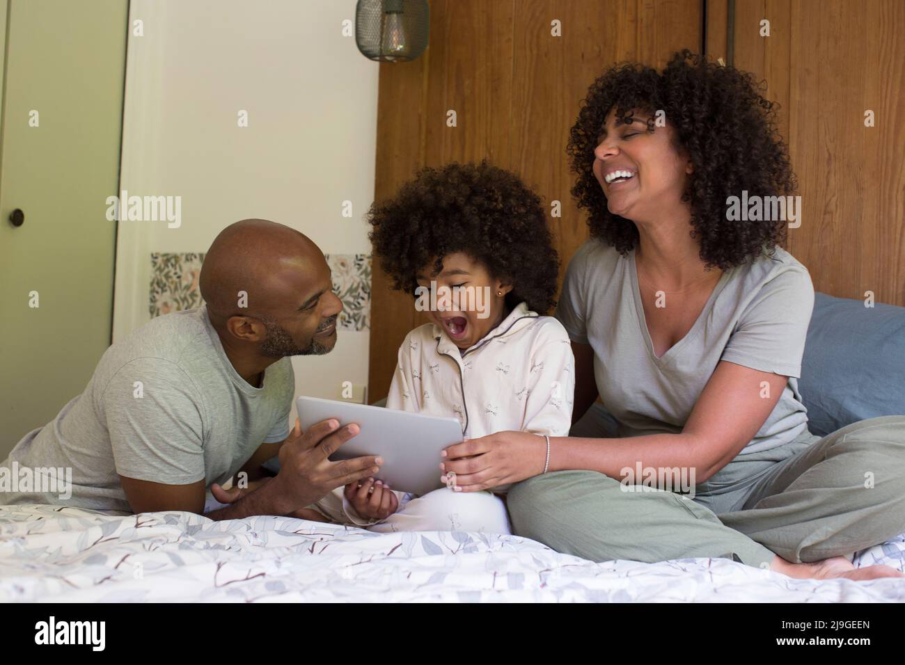 Eltern mit Tochter, die im Schlafzimmer ein digitales Tablet benutzen Stockfoto