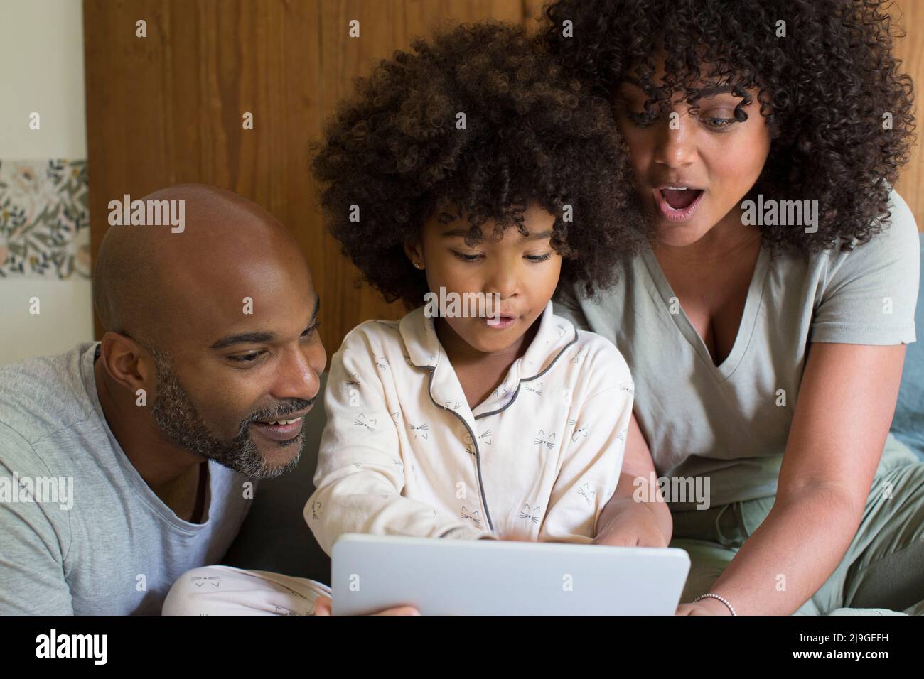 Eltern mit Tochter, die im Schlafzimmer ein digitales Tablet benutzen Stockfoto