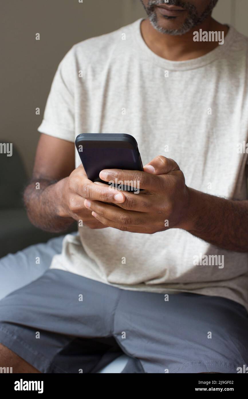 Mann mit Smartphone, während er im Schlafzimmer sitzt Stockfoto