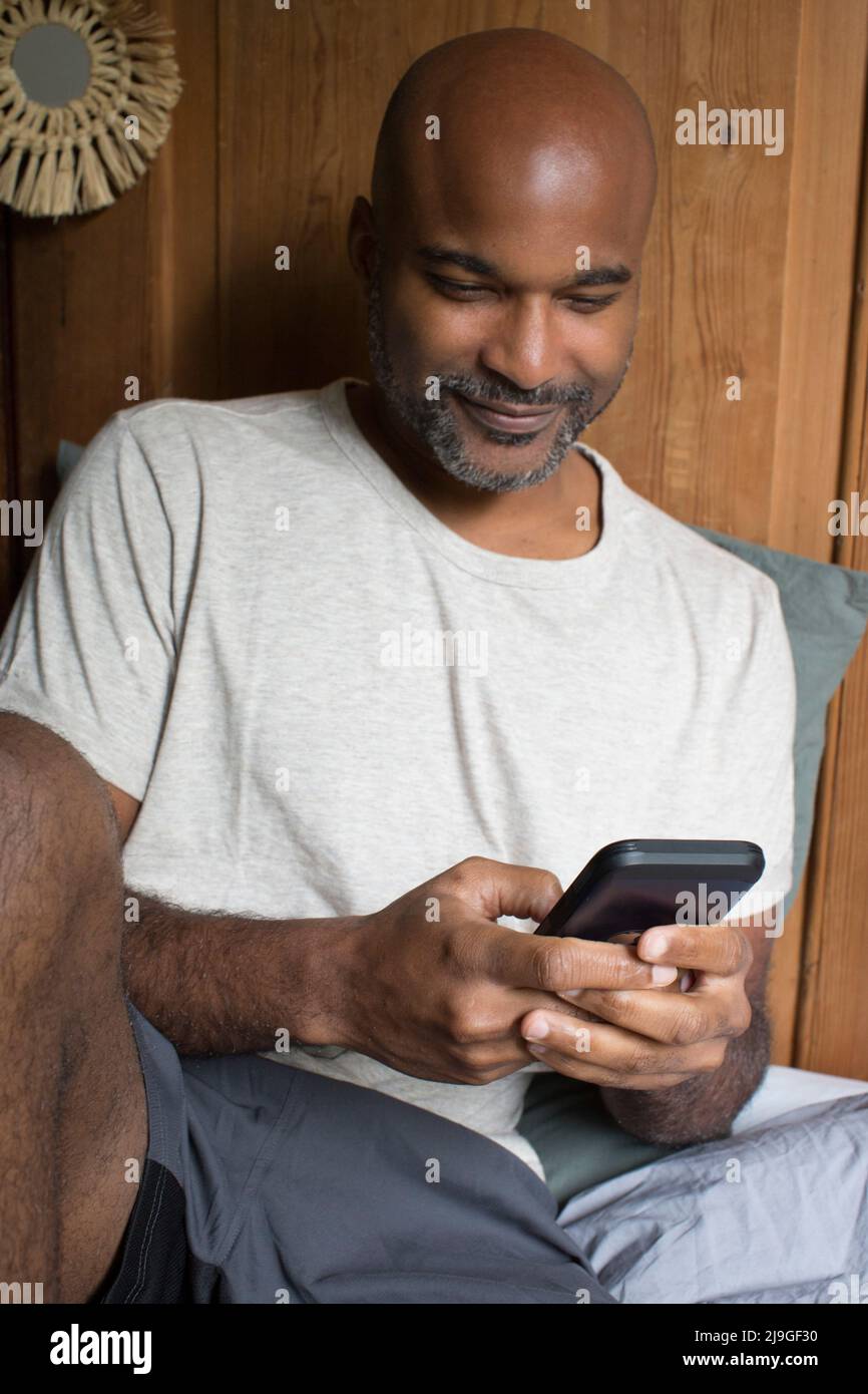 Mann mit Smartphone, während er im Schlafzimmer sitzt Stockfoto