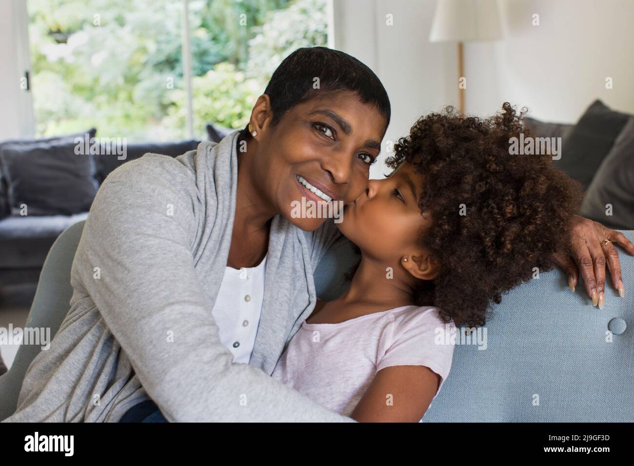 Enkelin küsst Großmutter im Wohnzimmer Stockfoto