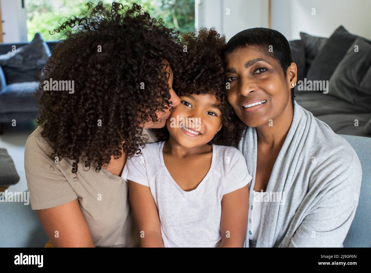 Lächelnde Großmutter und Enkelin schauten auf die Kamera, während die Mutter ihre Tochter küsste Stockfoto