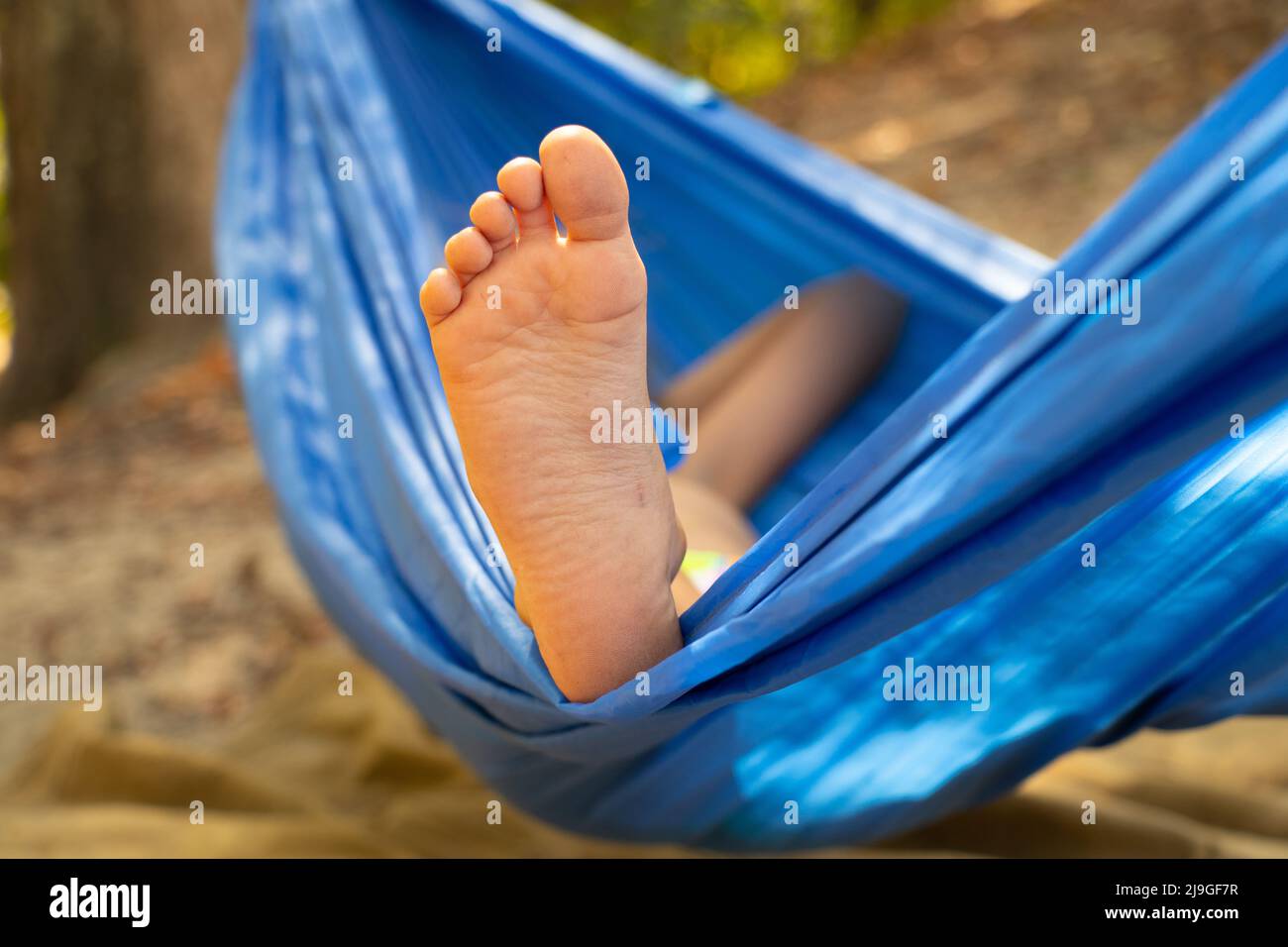 Kinderfuß in einer Hängematte, rollend im Wald im Sommer in der Sonne, Rest in einer Hängematte, ein Fuß in einer Hängematte, Rest im Wald Stockfoto