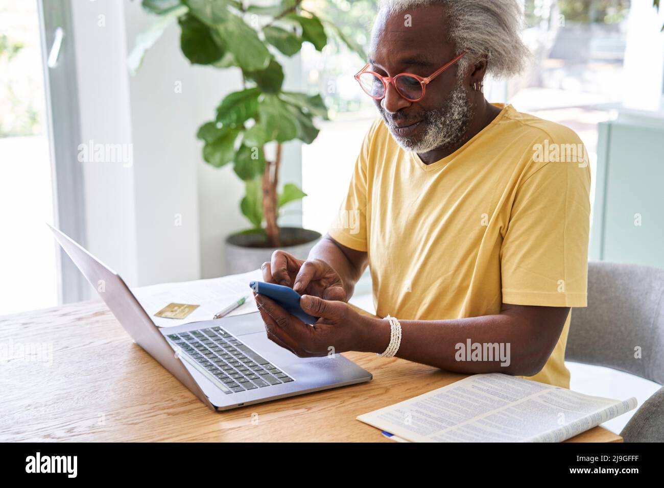 Älterer Mann mit Smartphone und Laptop Stockfoto
