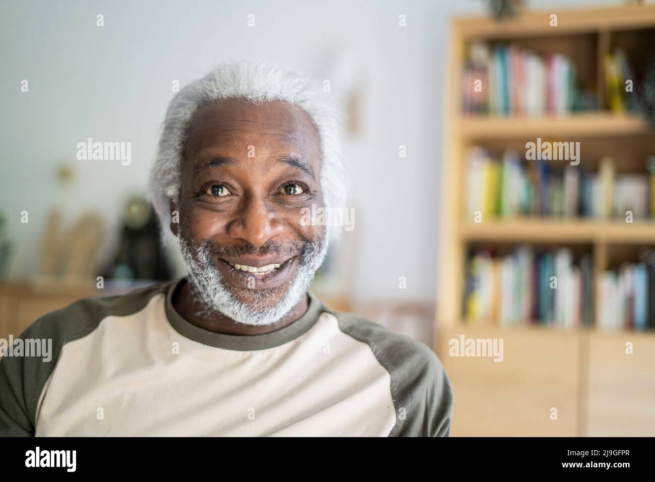 Lächelnder älterer Mann, der im Wohnzimmer sitzt Stockfoto
