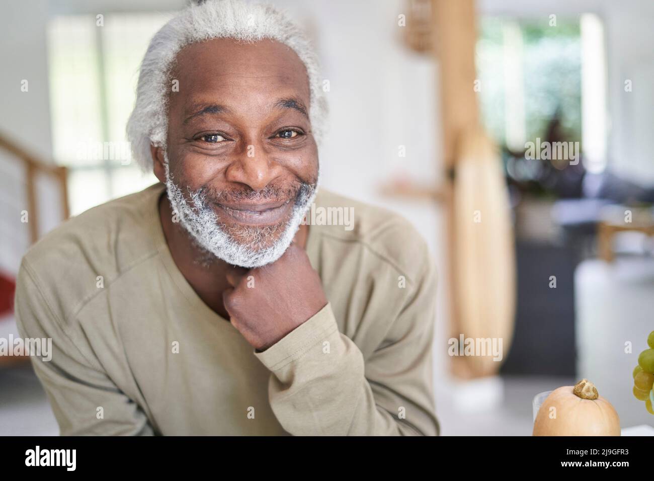 Lächelnder älterer Mann, der sich an der Küchenarbeitsfläche lehnte Stockfoto