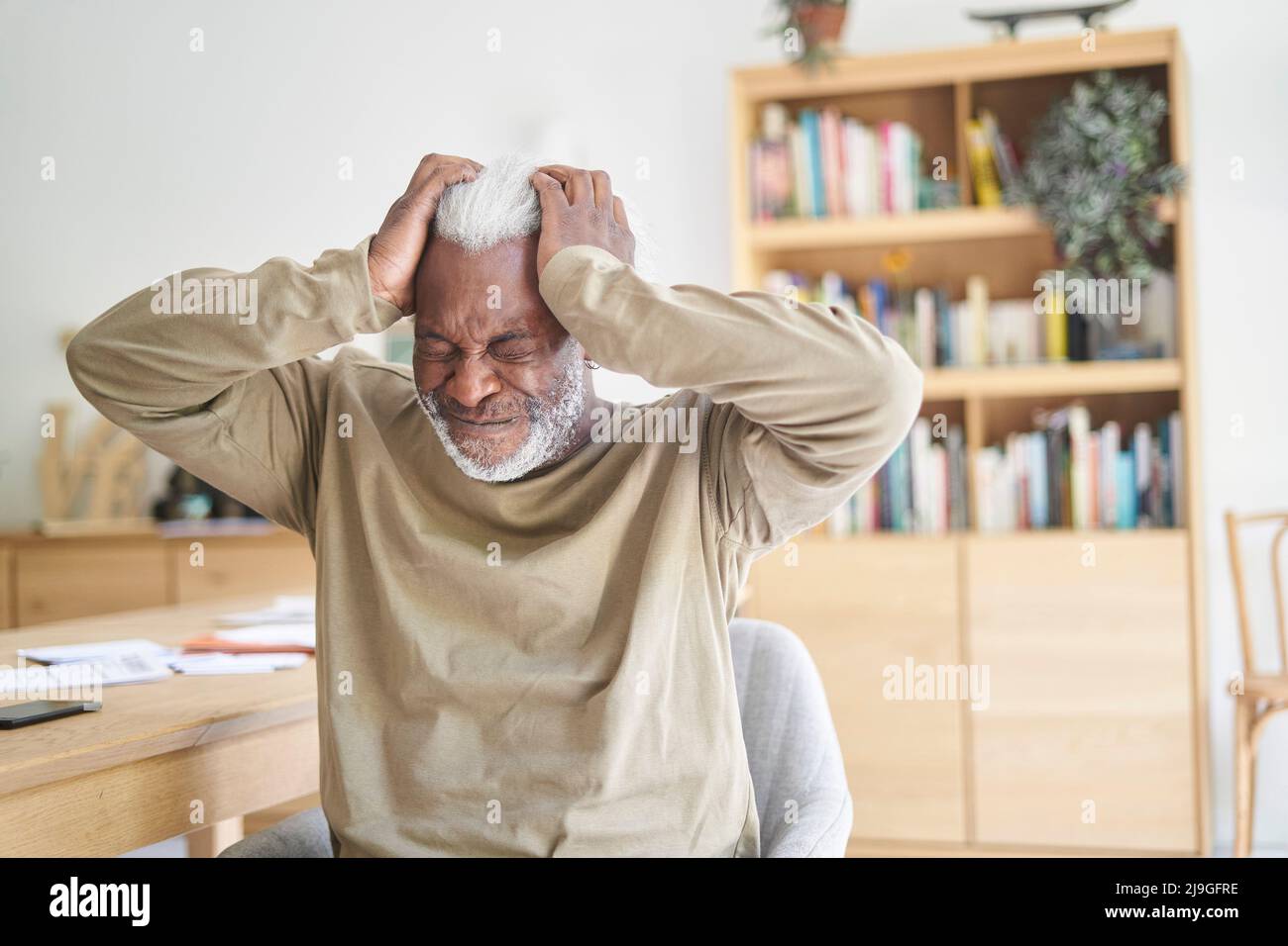 Älterer Mann, der im Wohnzimmer sitzt und unter Kopfschmerzen leidet Stockfoto