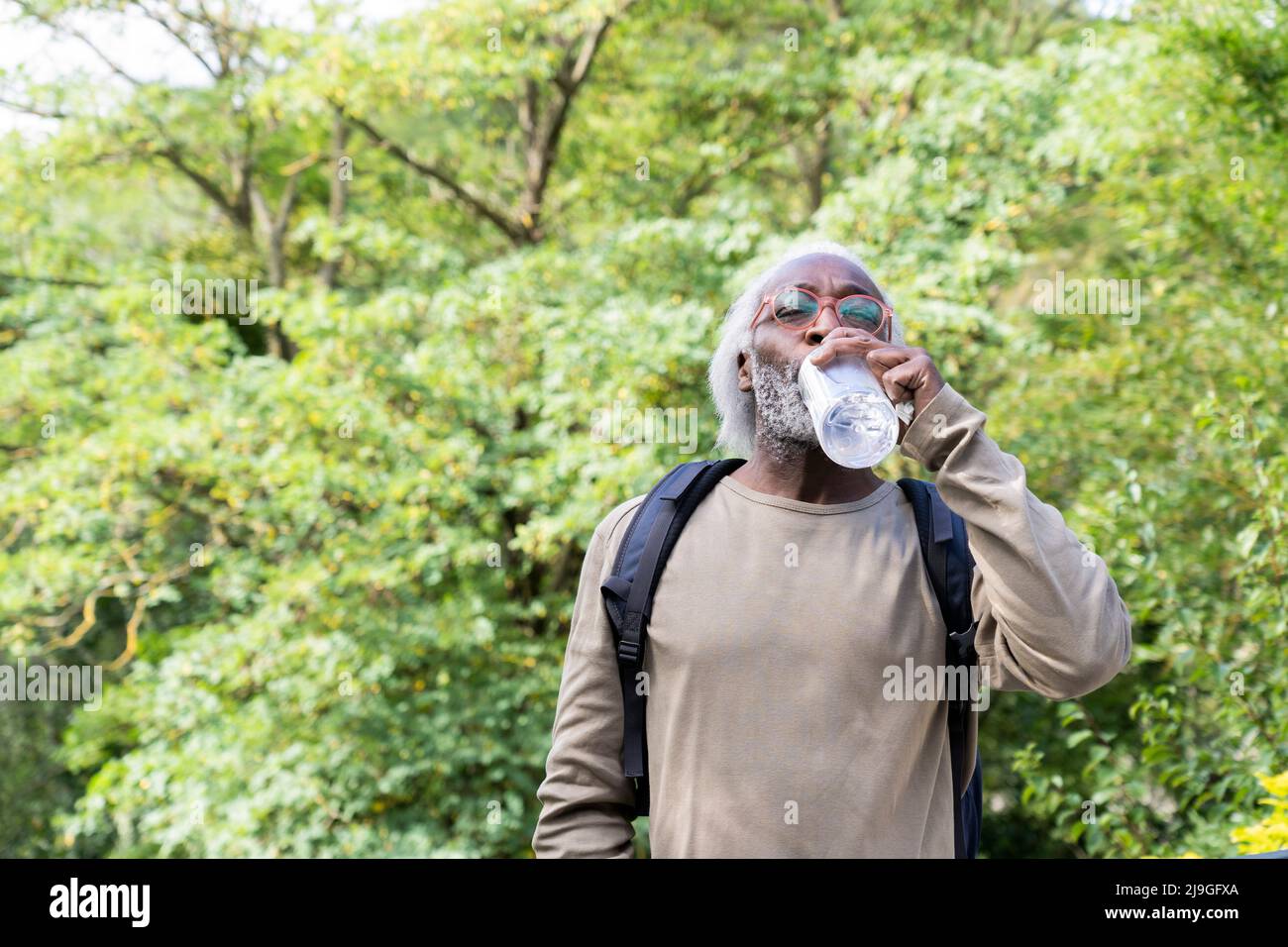Älterer Mann, der mit geschlossenen Augen Wasser trinkt Stockfoto