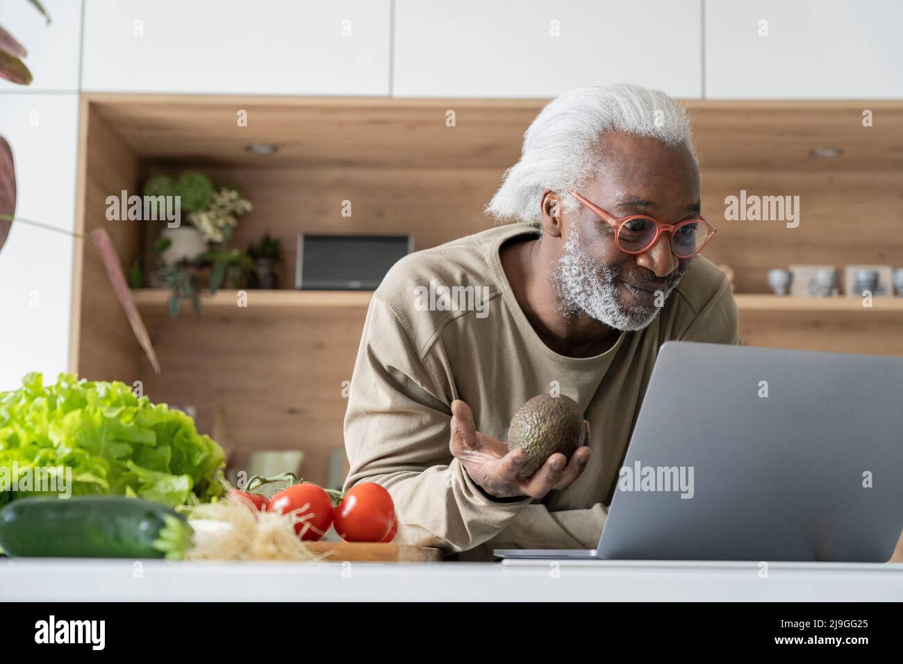 Ein älterer Mann schaut sich das Rezept auf dem Laptop an, während er sich auf die Küchenarbeitsfläche stützt Stockfoto