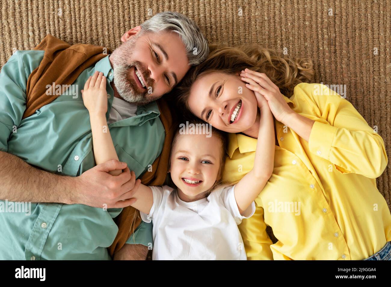 Glückliche Familie Umarmt Sich Auf Dem Boden Liegend Und Lächelt Vor Der Kamera In Der Halle Stockfoto