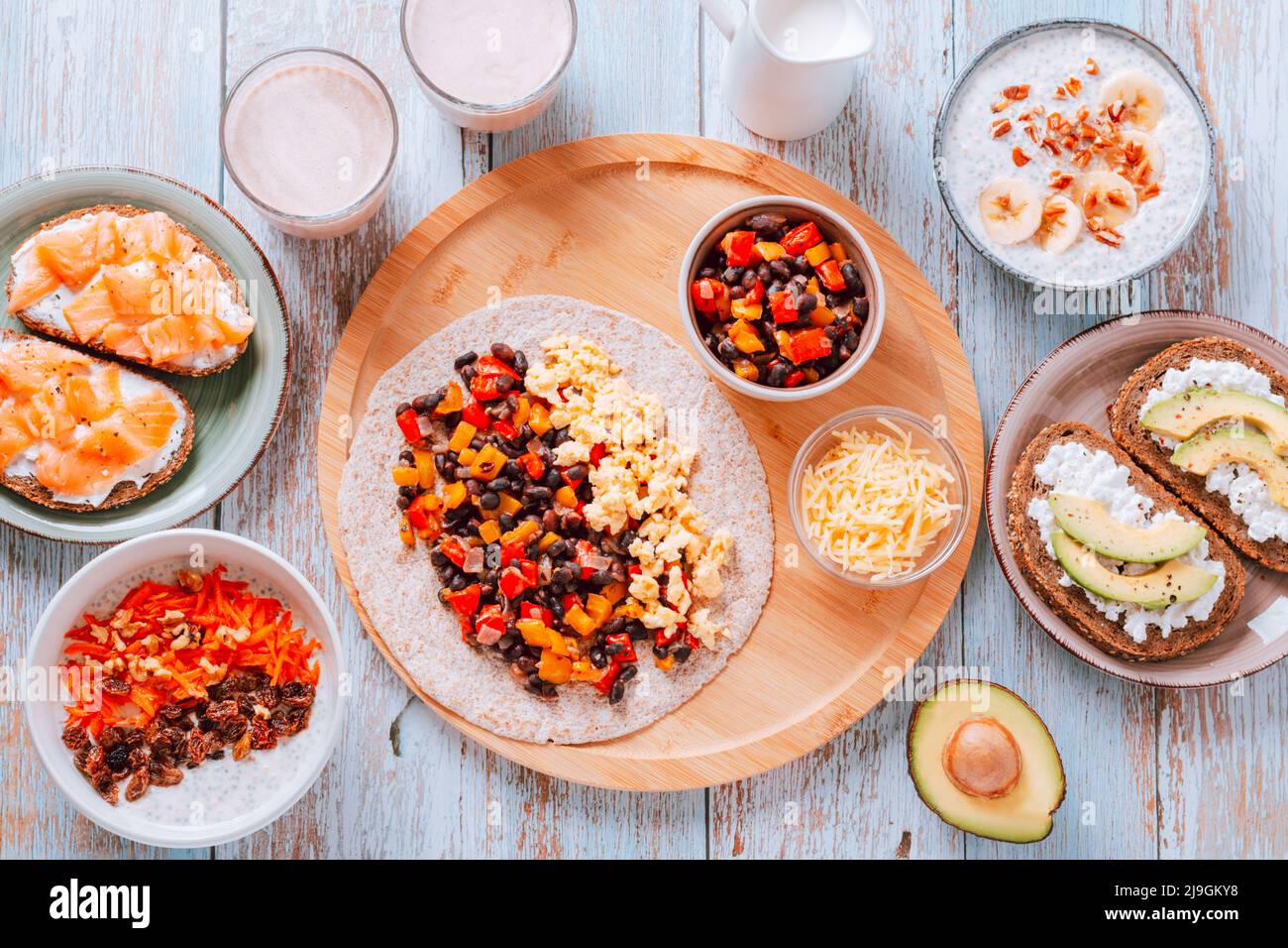 Bohnen und Eier Burritos, geräucherter Lachs und Avocado-Toast, Hafer mit Früchten und Nüssen, Erdnussbutter-Milchshake auf Holztisch. Gesund hoch Stockfoto