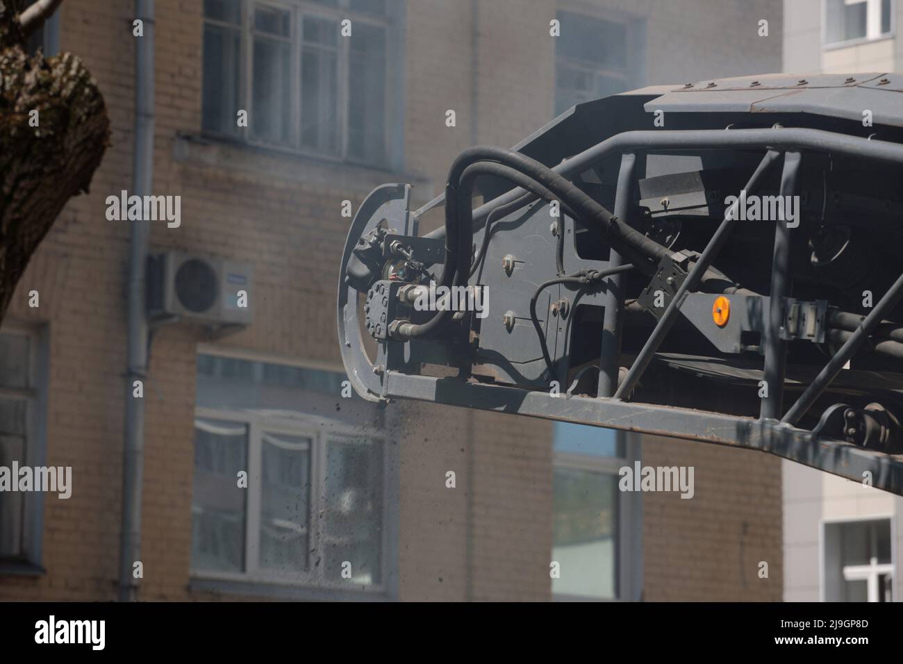 Das Straßenfräsfahrzeug lädt gefrästen Asphalt in einen Muldenkipper in einem engen Innenhof mit alten Häusern. Stockfoto