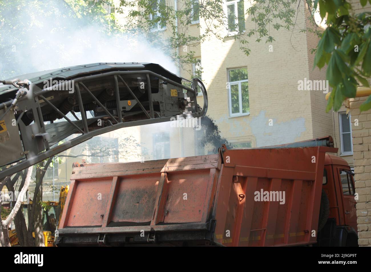 Straßenfräsfahrzeug entfernt alten Asphalt und lädt gefrästen Asphalt in Muldenkipper in einem engen Innenhof mit alten Häusern. Straßenreparaturarbeiten. Stockfoto
