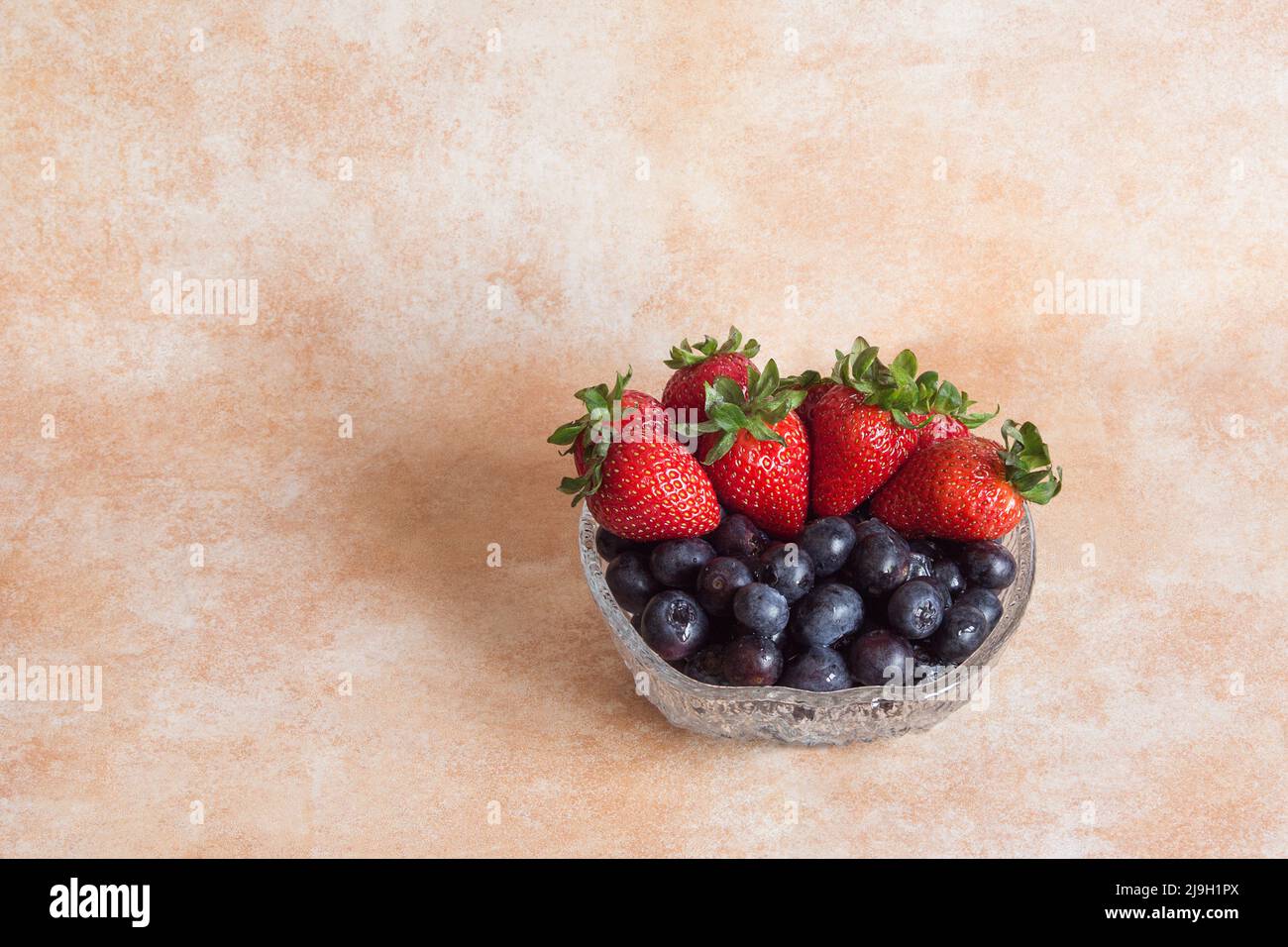 Glasschale mit frischen Erdbeeren und Blaubeeren auf einem abstrakten Hintergrund aus Pastellfarben und Kopierraum. Obst und Essen. Stockfoto