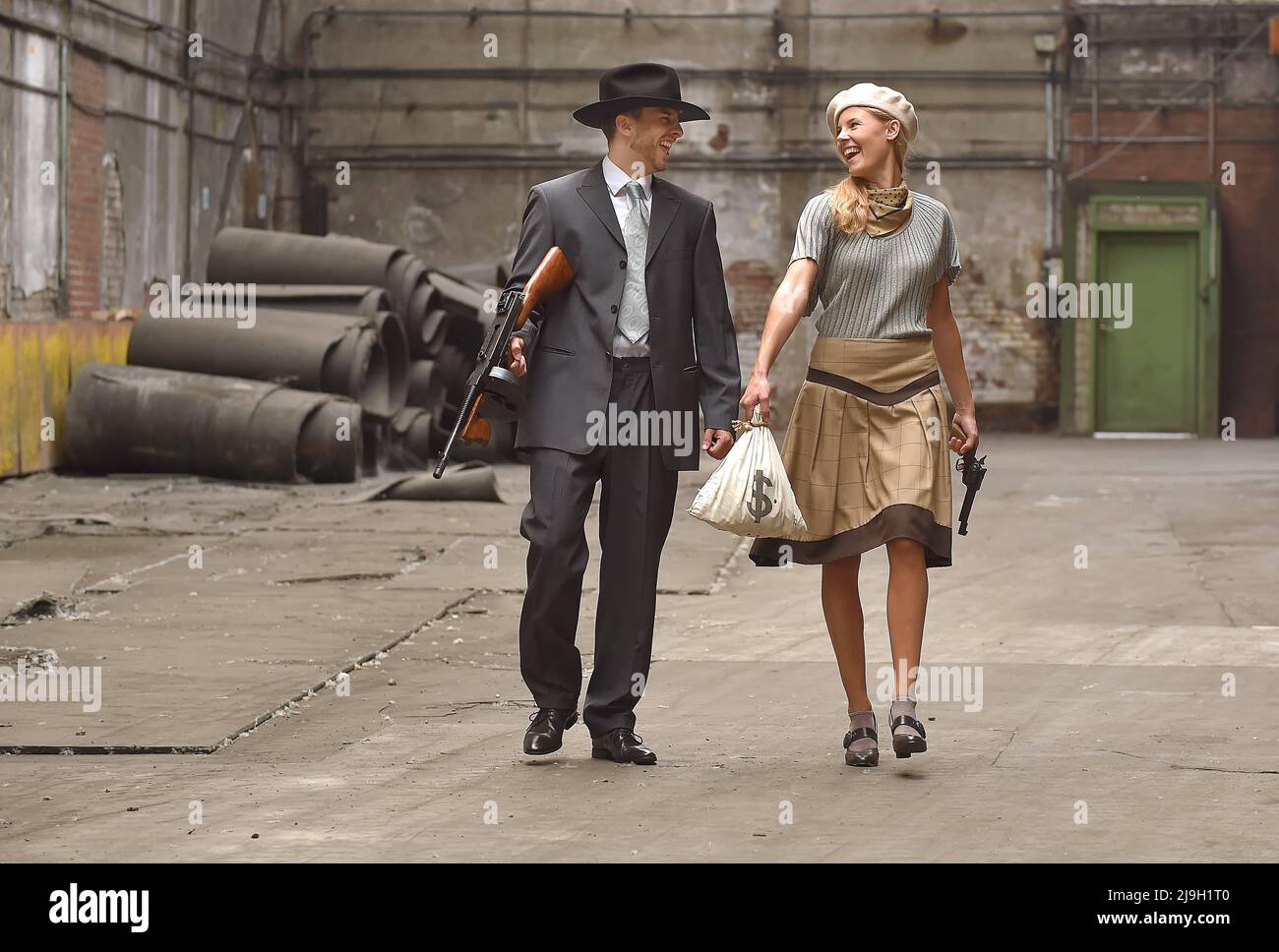Ein junges Paar zieht sich in Kleidung im Stil von 1930 an. Sie tragen jeweils eine Waffe, während sie die Rolle des berühmten Gangsterduos Bonnie und Clyde übernehmen. Stockfoto