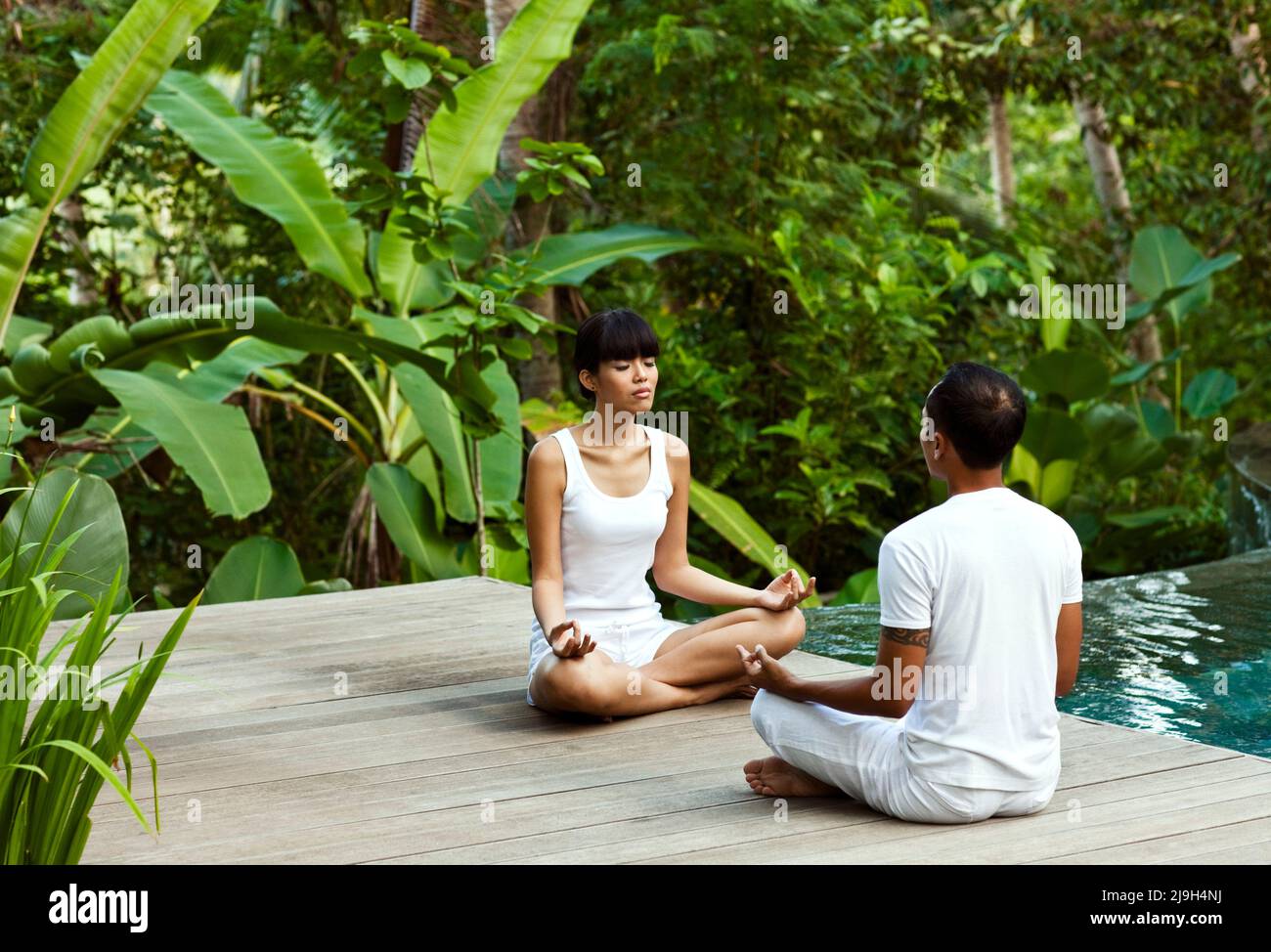 Eine junge asiatische Frau meditiert mit einem Yogalehrer in einer privaten Pool-Villa in Kayumanis Ubud, Bali, Indonesien. Stockfoto