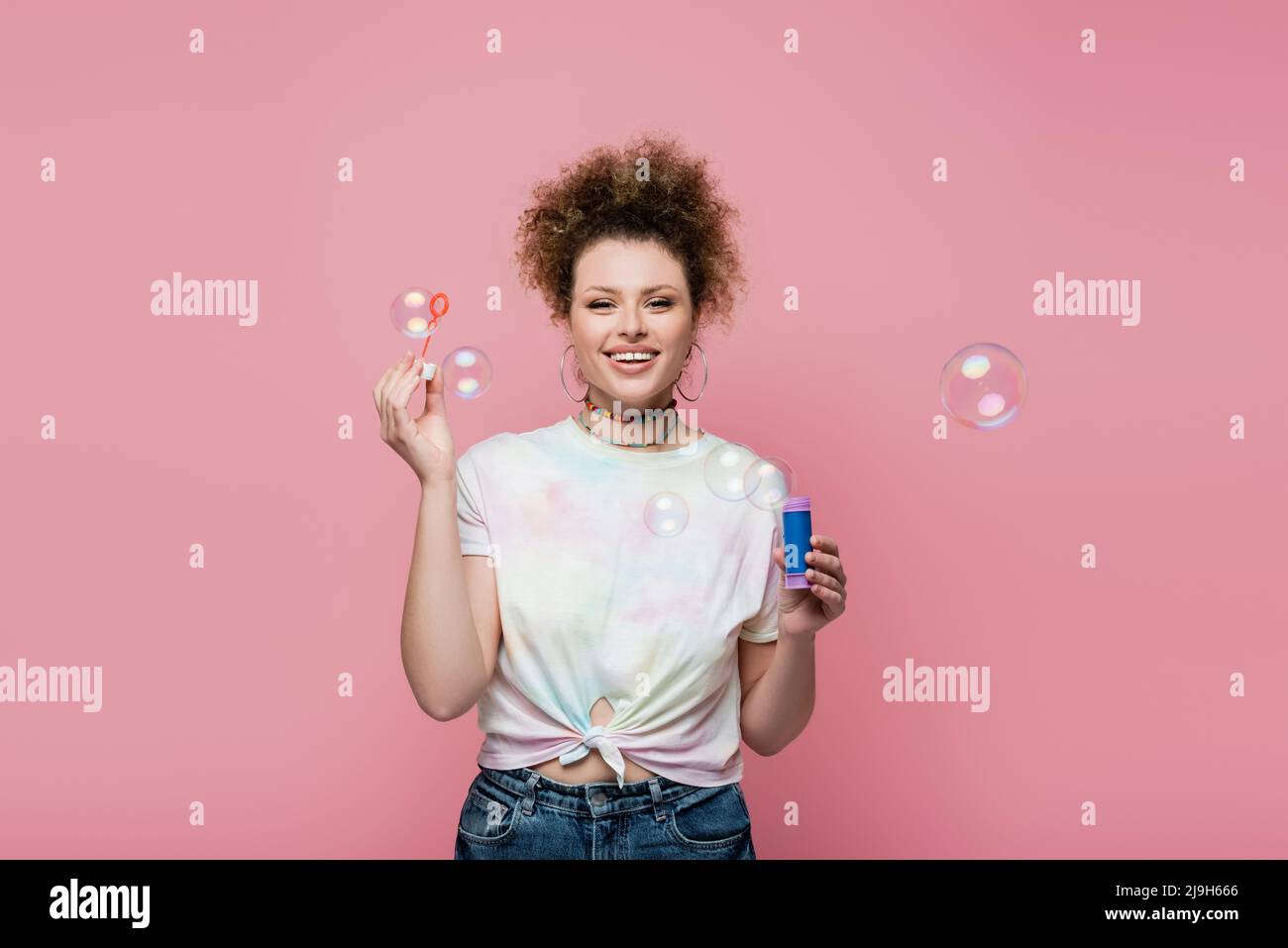 Lächelnde Frau hält Seifenblasen auf rosa Hintergrund Stockfoto