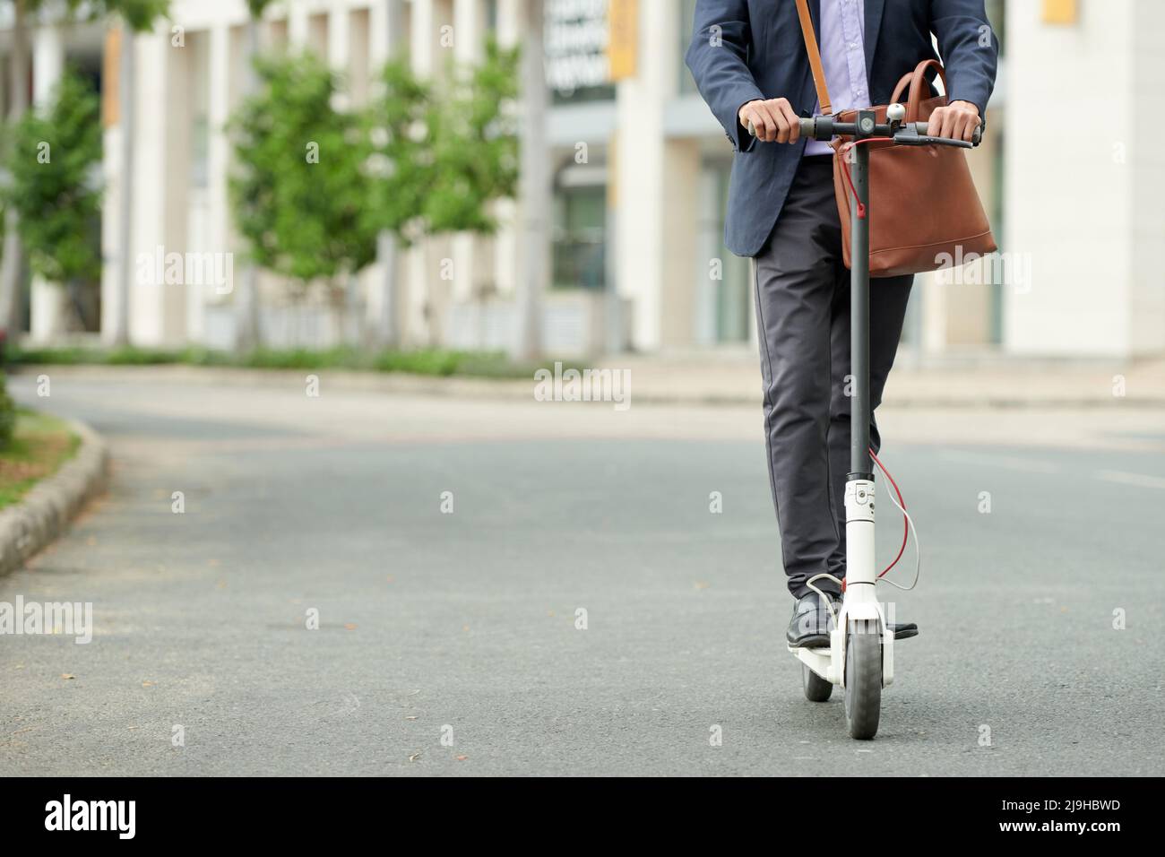 Beschnittenes Bild eines Unternehmers in Anzug, der auf einem E-Scooter zu einem Geschäftstreffen fährt Stockfoto