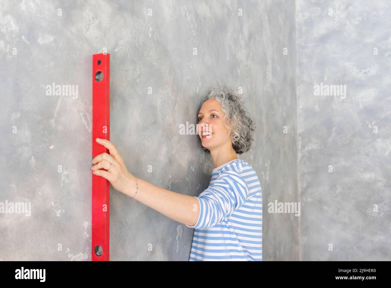 Lächelnde Frau mit einem Füllstandmessgerät an der grauen Wand Stockfoto