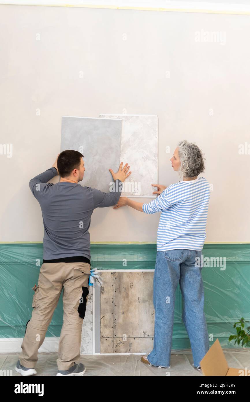 Frau und Freund wählen Tapete aus Proben auf weißer Wand Stockfoto