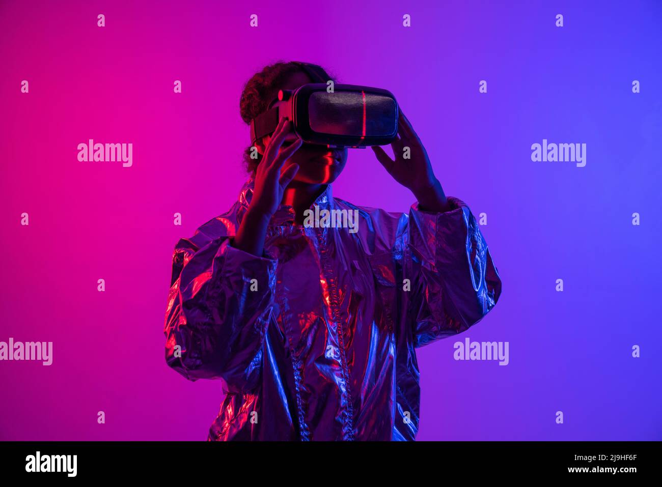 Junge Frau trägt Virtual-Reality-Simulator steht vor mehrfarbigem Hintergrund Stockfoto