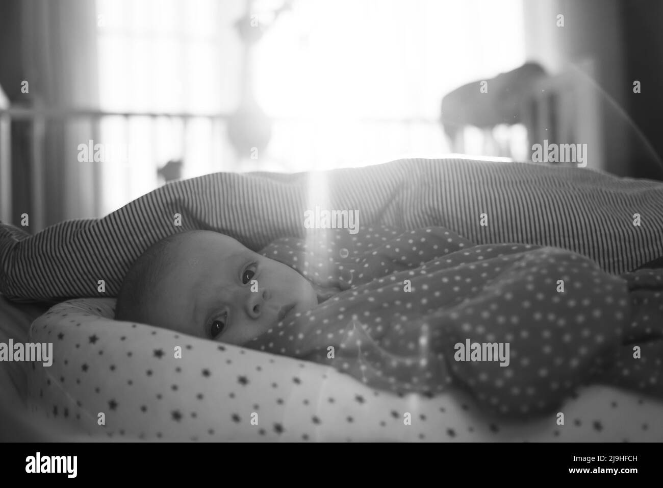 Niedlicher kleiner kaukasischer Junge, der am Bett liegt und die Kamera anschaut Stockfoto